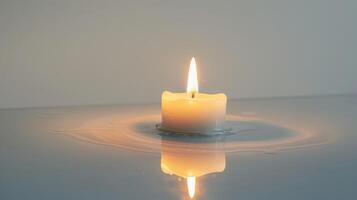 White candle floats on calm water, casting a soft glow and creating ripples. photo