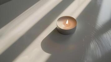Lone scented candle flickers on a white table, casting shadows in the soft window light photo