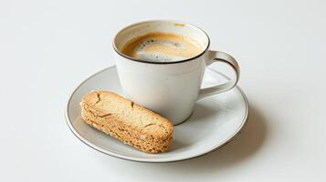 Frothy crema-topped cup of coffee and a single biscotti cookie rest on a white table photo