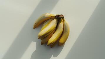 Bananas creating long shadows on a simple white table with space for text photo