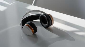 Modern wireless headphones with black earcups and a white headband rest on a white table. photo