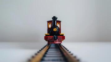 Vibrant red toy train on miniature railroad track, against clean white background photo