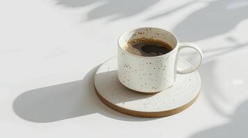 Cup of coffee sits on a white table, casting shadows from the sun shining through a nearby window photo