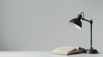 Book illuminated by a black desk lamp on a white table against a grey backdrop photo