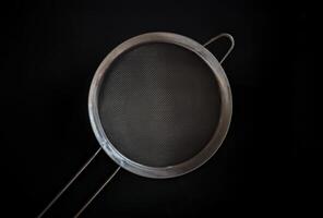 A metal mesh strainer on a black background, concept of a kitchenware photo