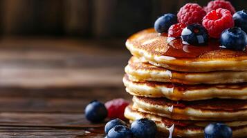 Close-up of a stack of golden-brown pancakes drenched in maple syrup, topped with fresh blueberries and raspberries, with a rustic wooden background photo