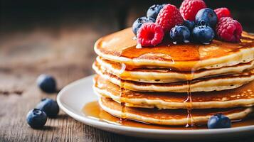 Close-up of a stack of golden-brown pancakes drenched in maple syrup, topped with fresh blueberries and raspberries, with a rustic wooden background photo