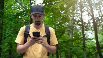 Face man with backpack in forest uses phone to touch the screen looking for connection signal video