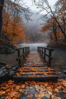 A rustic wooden bridge crossing a calm river in the middle of a dense autumn forest, golden leaves floating on the water, mist rising from the cool air photo