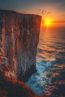A picturesque coastal cliffside with waves crashing against the rocks below, seagulls flying overhead, the sun setting over the distant horizon, casting a golden glow photo
