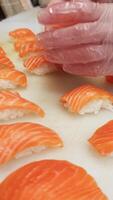 Japanese cuisine master prepares salmon nigiri close-up in vertical , shaping each nigiri with precision. The delicate process of making nigiri showcases authentic culinary artistry. video