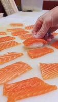 Vertical of Japanese cuisine master crafting salmon nigiri close-up, focusing on the precise creation of each nigiri piece. The chef's hands skillfully form the traditional nigiri shape. video