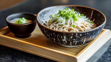 A bowl of chilled zaru soba noodles served on a bamboo tray with a small dish of dipping sauce, garnished with finely chopped green onions and grated daikon photo