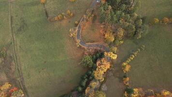 Aerial view of car driving on country road winding through autumn forest in mountains. Natural landscape in fall season video