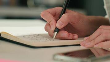 Person is sketching in notebook while working remotely at desk with laptop. Freelance work at home office. Graphic designer drawing sketch video