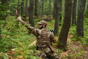 An elite soldier, camouflaged and stealthily navigating through dangerous woodland terrain, executes a covert mission in a secluded forest area photo