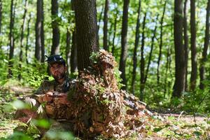 A skilled sniper and a soldier operating a drone with VR goggles strategize and observe the military action while concealed in the forest photo