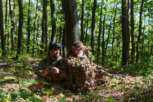 A skilled sniper and a soldier operating a drone with VR goggles strategize and observe the military action while concealed in the forest photo