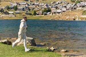 Athletic man maintains his healthy lifestyle by running through the scenic mountain and lakeside environment, showcasing a commitment to fitness and well-being photo