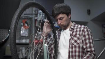 Bicycle repair in workshop. Man bike mechanic fixes wheel, tension spokes with special tool on stand for adjusting wheels. Handyman fixes wheel spokes by working in cycle service station. video