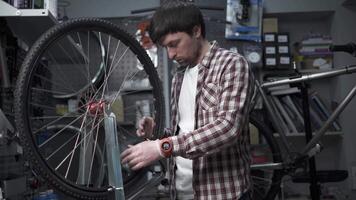 Wheel straightening stand in bicycle workshop. Mechanic uses tool to tension spokes in rim of velocipede. Small business bike repair and service theme. Truing cycle wheel. Cycle mechanic fixes wheel. video