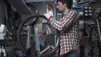 Bicycle repair in workshop. Man bike mechanic fixes wheel, tension spokes with special tool on stand for adjusting wheels. Handyman fixes wheel spokes by working in cycle service station. video