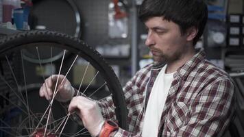 Bicycle repair in workshop. Man bike mechanic fixes wheel, tension spokes with special tool on stand for adjusting wheels. Handyman fixes wheel spokes by working in cycle service station. video