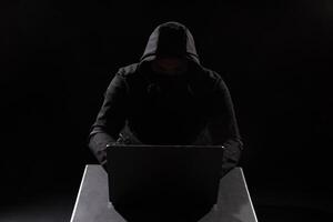 Cyber hacker in hood behind laptop in dark room, digital cyber security concept, Computer hacking photo