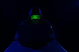 Cyber hacker, digital cyber security concept, hooded hacker behind laptop on dark background photo