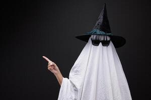 Person in costume of ghost pointing at something on dark background with space for tex photo