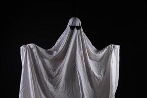 Person in costume of ghost pointing at something on dark background with space for tex photo