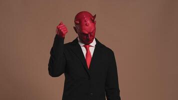 Red devil businessman with horns knocking himself on the head and shaking his head negatively demonstrating misunderstanding in the studio on a brown background video