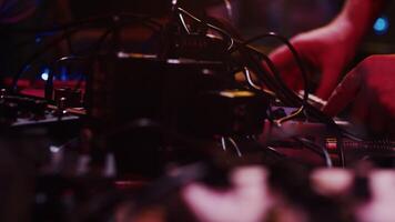 Sound engineer adjusting the settings of a controller surrounded by many electronic devices and wires during the show under concert lights close up video