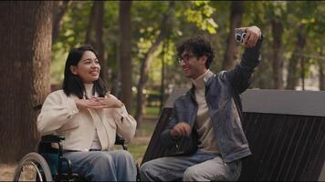Young man showing smartphone to girlfriend using wheelchair in park video
