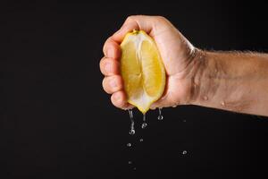 Squeezing fresh lemon juice on dark background, hand squeezing fresh lemon juice close up photo