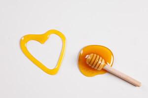 honey spoon with spilled honey in the shape of a heart on a white background top view photo
