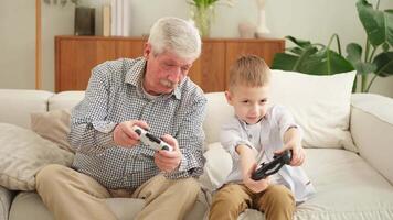 Happy family. Old senior man grandfather boy grandson playing game with joysticks at home. Smiling grandparent and child using gamepads for game. Older generation modern tech usage video