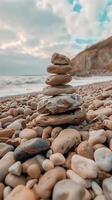 Stack of smooth stones on pebbly beach. Calm sea waves and cliffs under cloudy sky, serene photo