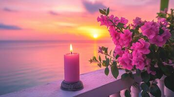 A pink candle and vibrant flowers on a balcony overlook a serene sunset photo
