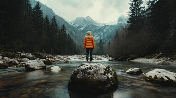 woman standing on rocks in river, surrounded by mountains forest. photo