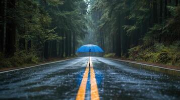 Blue umbrella in heavy rain on a wet road with a natural forest backdrop photo
