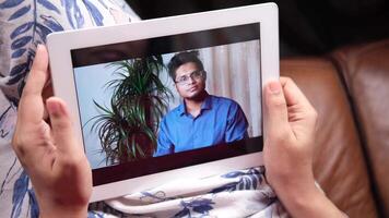 A man is seen on a tablet computer in a call with his family video