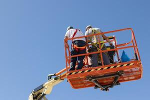 Low angle view of a Two workers on a cherry picker with safety equipment on a sunny day. Copy space photo