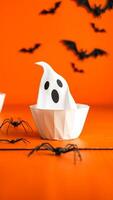Halloween Ghost in a Bowl with Bats and Spiders on an Orange Background photo