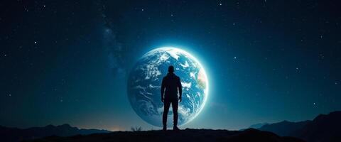 Silhouette of a man standing on a mountain range with a glowing Earth in the sky photo