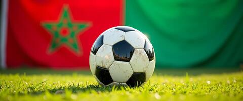 Soccer ball on green grass with Moroccan flag in background photo