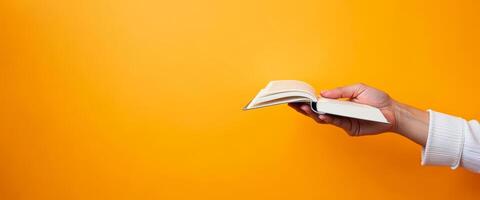 Hand Holding Open Book Against Yellow Background photo