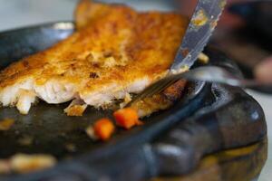 Close up of Cutting or slicing the dori steak on grill plate with knife and fork photo