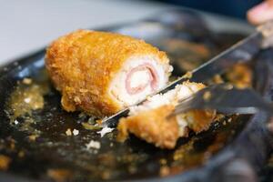 Close up of sliced chicken cordon blue with knife and fork on grill plate photo