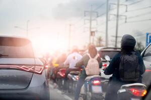 Rear side of luxury grey car with turn on brake light. Beside with many motorcycle and driver. stop and stuck in working time. Environment of air pollution. Beside road with electric pole. photo